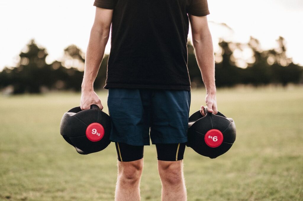 Man exercising outdoors with medicine balls in a park setting, promoting fitness and strength.